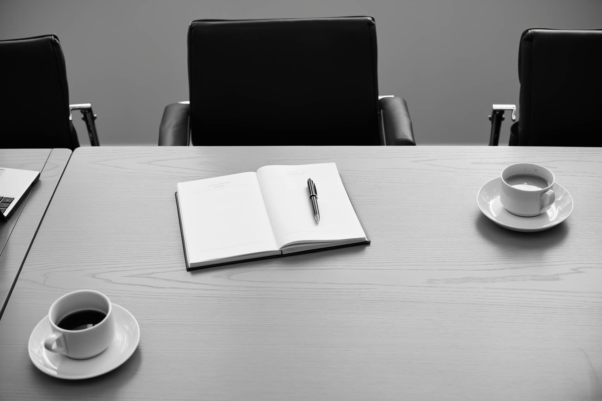 Een vergadertafel van bovenaf met een notitieblok, een pen en twee kopjes koffie
